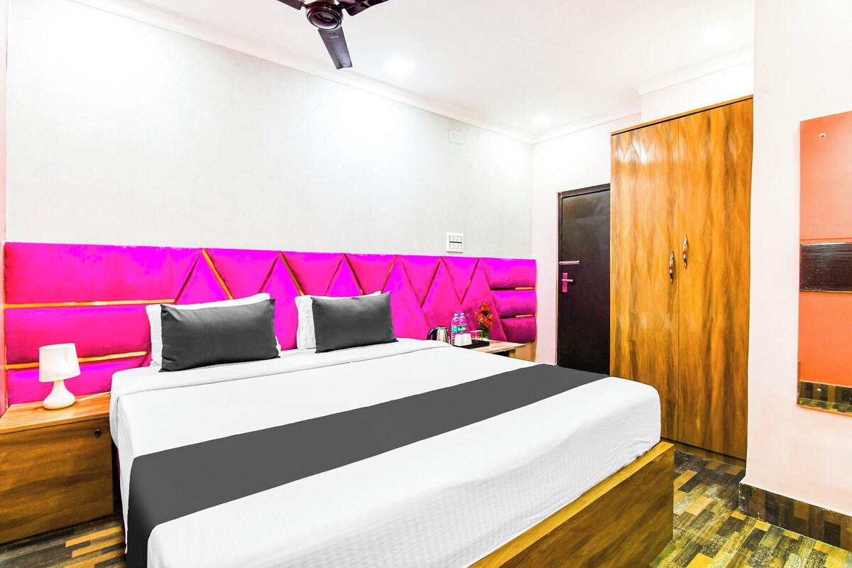 A hotel room with a bed, a nightstand, a lamp, a water bottle, and a wooden wardrobe.