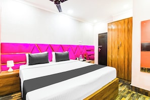 A hotel room with a bed, a nightstand, a lamp, a water bottle, and a wooden wardrobe. - Hotel O Barsana (Kolkata)