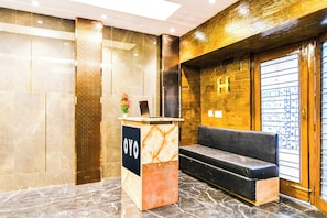 A reception area with a marble reception desk, a black sofa, and a wooden wall with a letter 'H'. - Hotel O Barsana (Kolkata)