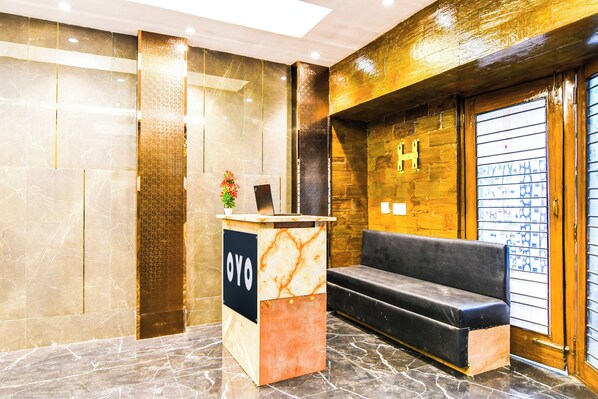 A reception area with a marble reception desk, a black sofa, and a wooden wall with a letter 'H'.