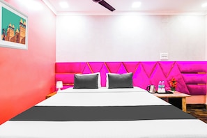 A hotel room with a bed, two pillows, a nightstand, a water bottle, a kettle, and a framed picture on the wall. - Hotel O Barsana (Kolkata)
