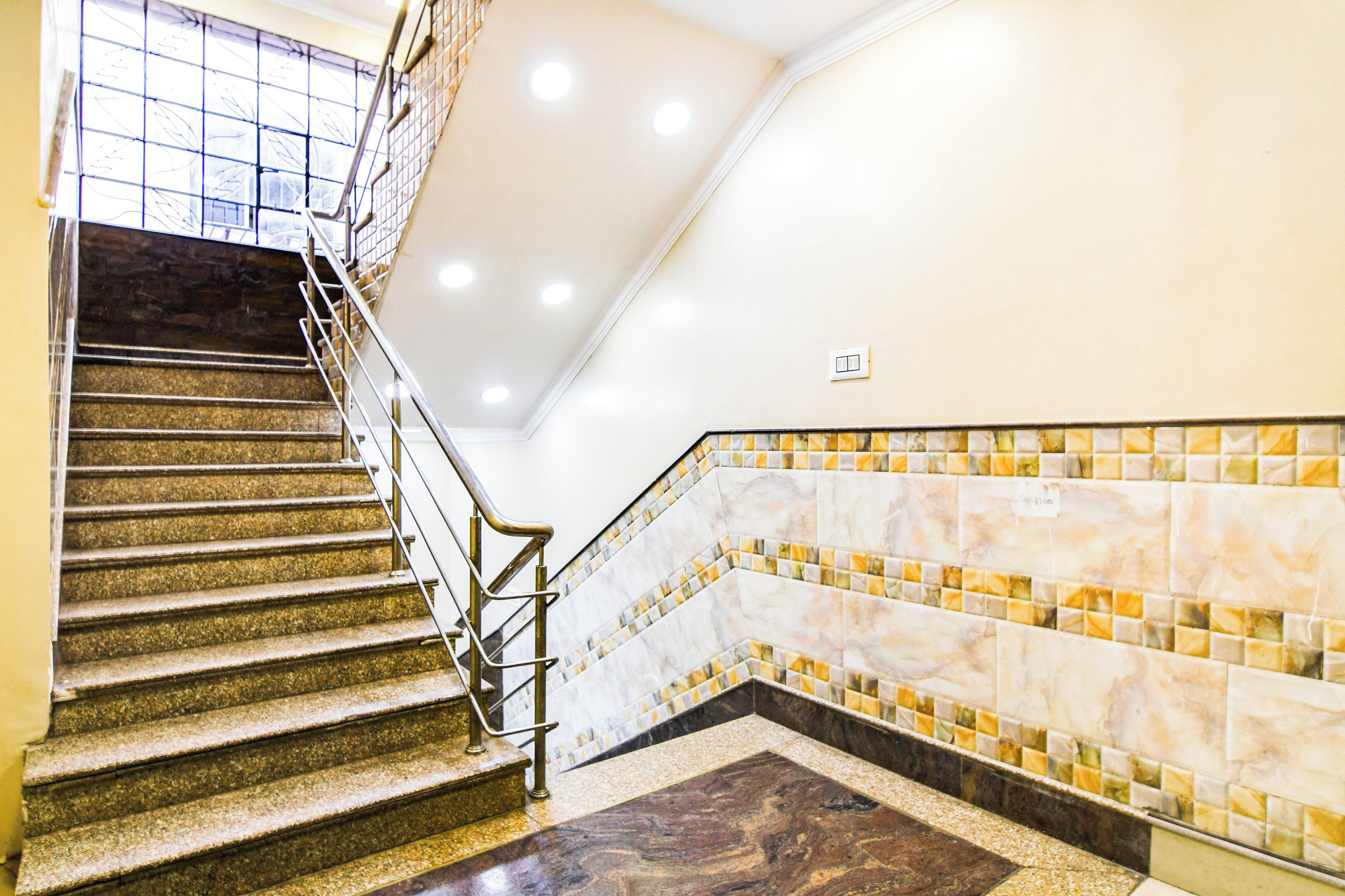 A staircase with a handrail, a tiled wall with a pattern, and a light switch on the wall.