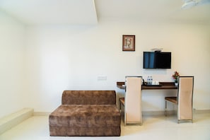 A furnished room with a sofa, a desk, a chair, a television mounted on the wall, and a small table with a vase of flowers. - Hotel O Eminent Hotel (Kolkata)