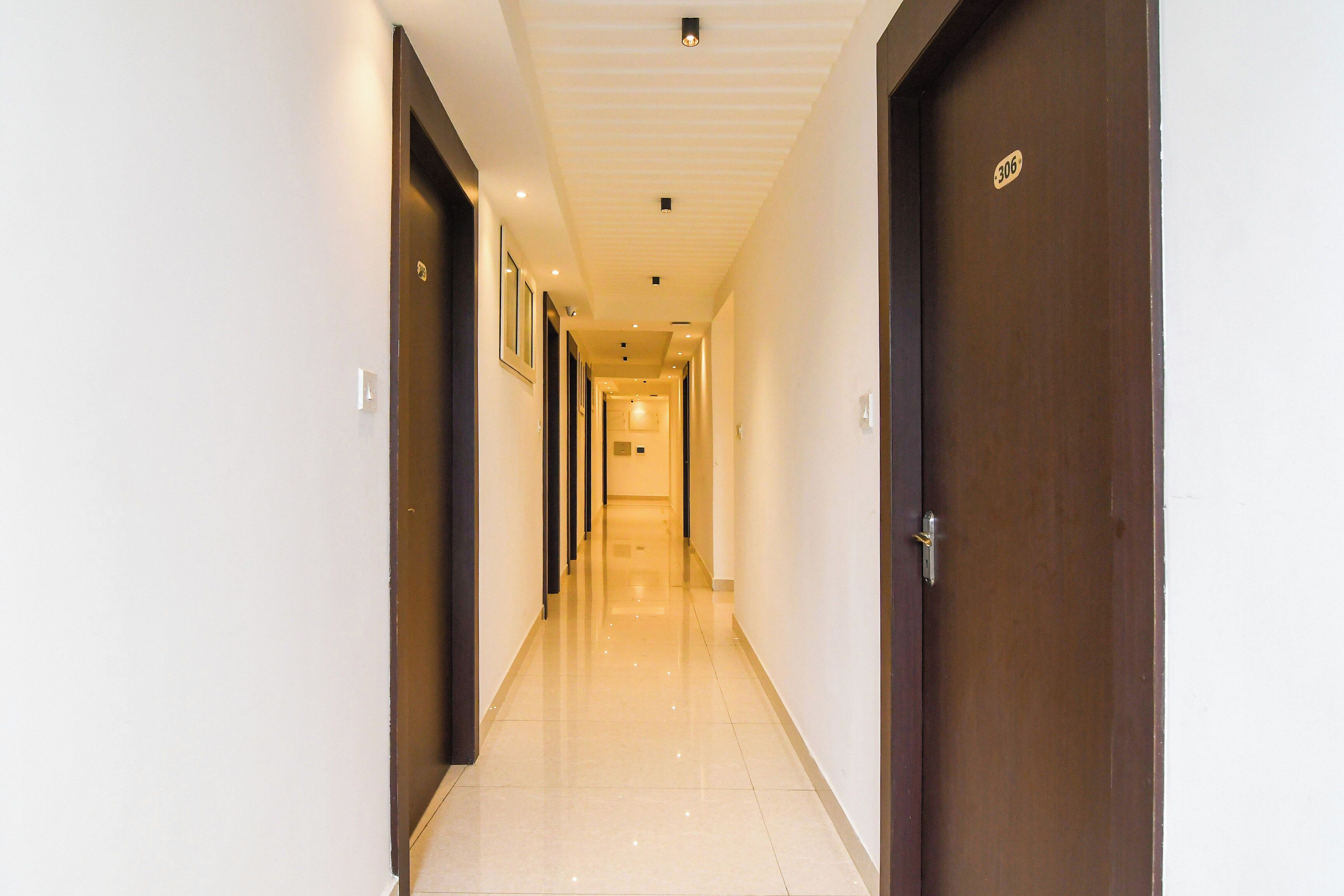 Un couloir d’hôtel avec des portes des deux côtés, un sol carrelé et des luminaires encastrés au plafond.