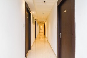 Un pasillo de hotel con puertas a ambos lados, piso de baldosas e iluminación empotrada en el techo.