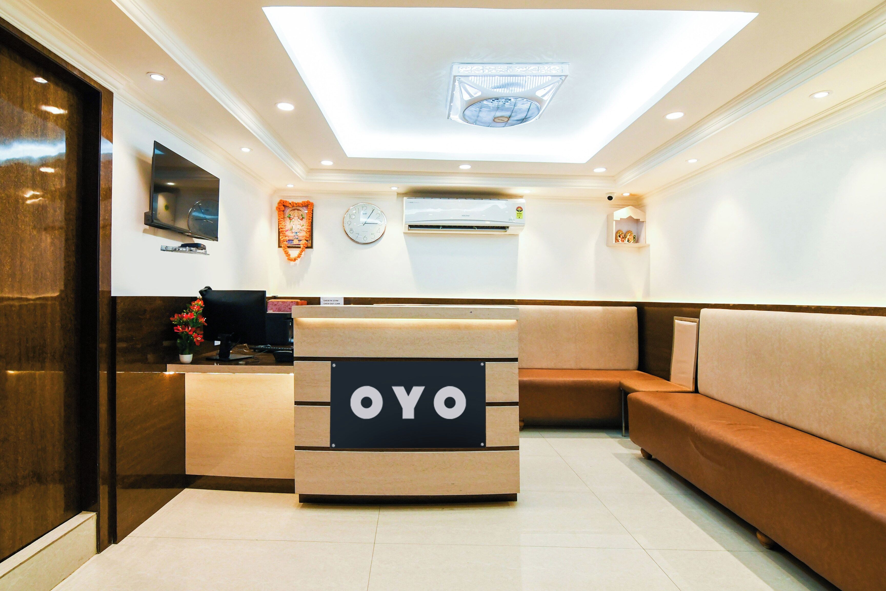 Un espace d’accueil comprenant un comptoir de réception portant l’inscription « OYO », une horloge, un appareil de climatisation et un téléviseur fixé au mur.