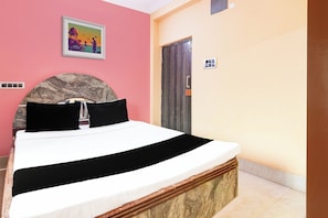 En säng med en sänggavel, en tavla på väggen, en dörr och en termostat.
