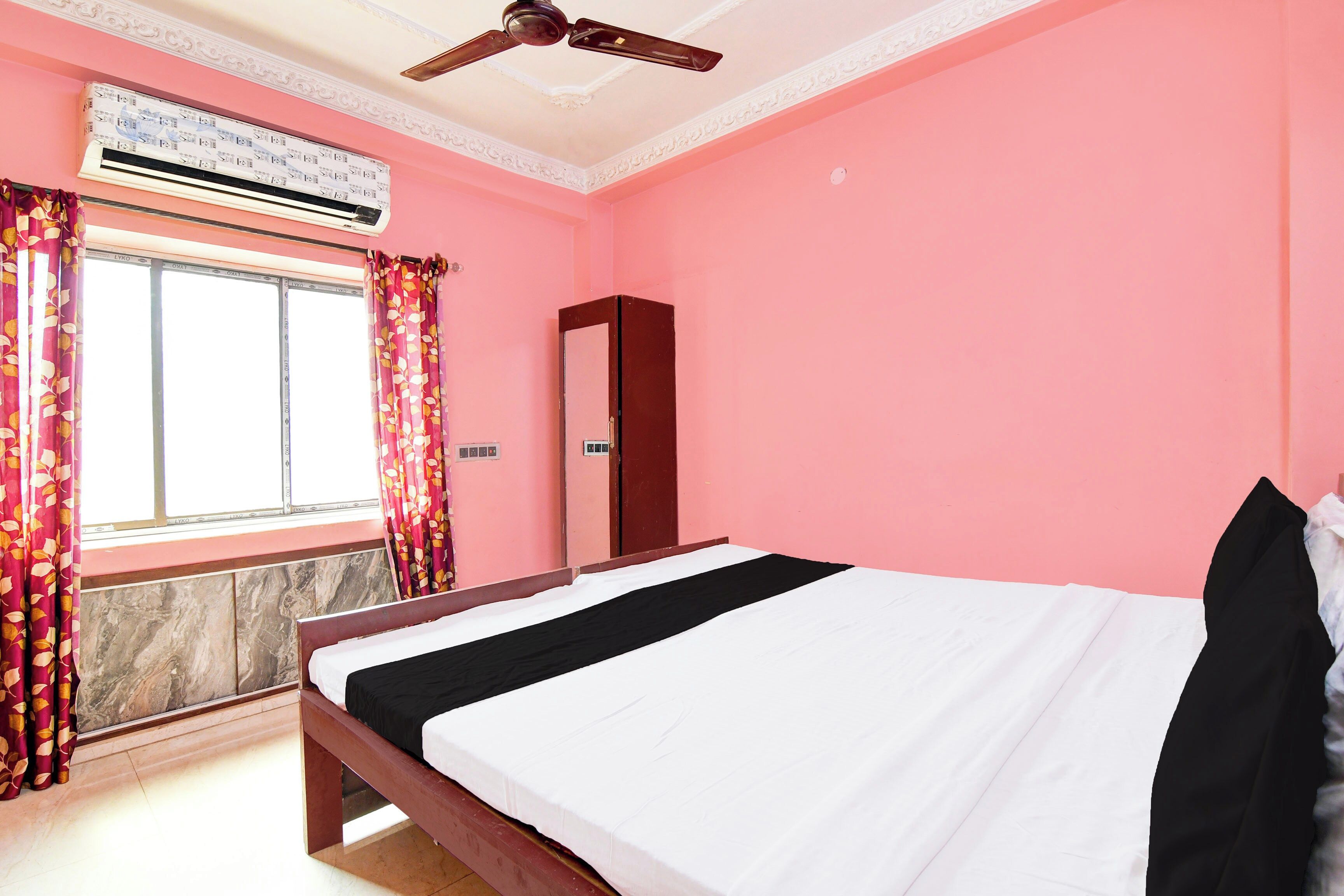 Un dormitorio con cama, armario, ventilador de techo, unidad de aire acondicionado y ventana con cortinas.