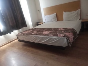 Ein Bett mit floralem Überwurf, einem hölzernen Kopfstück und einem Nachttisch mit Lampe.
