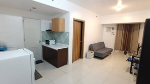 A compact living space with a kitchenette, a grey sofa, a small table, and a glass partition. - Grand Riviera Suite 1BR with 2 beds near SLEC & US EMBASSY (Manila)