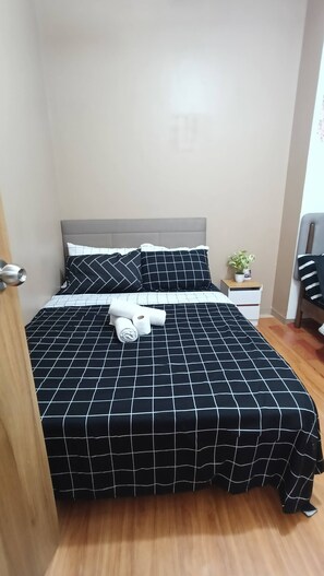 A neatly made bed with a black and white checkered bedspread, a pillow, and a rolled towel. - Grand Riviera Suite 1BR with 2 beds near SLEC & US EMBASSY (Manila)