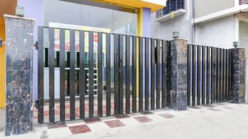 A gated entrance with a checkered floor pattern, a metal gate, and a building with a yellow and grey facade.