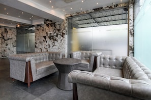 Ein moderner Lounge-Bereich mit einer Eckcouch, einem runden Korbtisch und einer Glastrennwand.