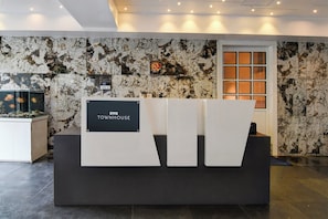 A reception desk with a sign reading 'TOWNHOUSE' in a lobby with a marble wall and a fish tank. - Collection O Water View Residency (Barasat)