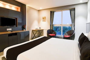 Ein Hotelzimmer mit einem Bett, einem Fernseher, einem kleinen Tisch mit Stuhl und einem Fenster mit Vorhängen.