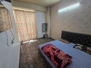 A bedroom with a bed, a television, a wall-mounted light, and a window with curtains. - Hotel O golden shiva (Amritsar)