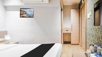 Une chambre d’hôtel avec un lit, une table de chevet avec une lampe, un tableau au mur, une armoire et une salle de bain visible à travers une porte ouverte.