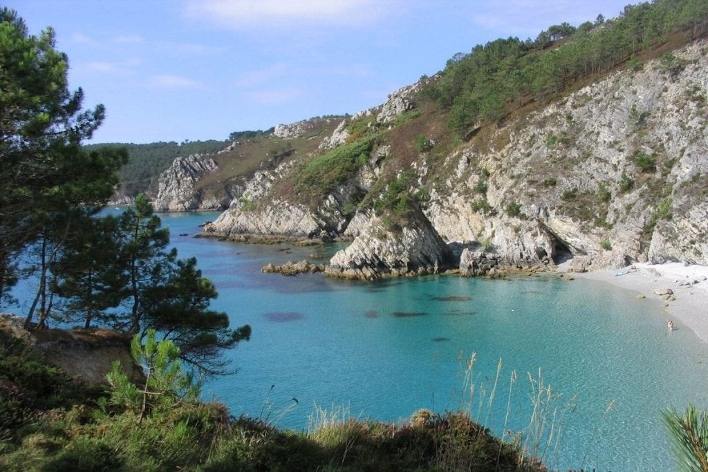 Un paysage côtier caractérisé par des falaises rocheuses, une eau d’un bleu limpide et une plage.