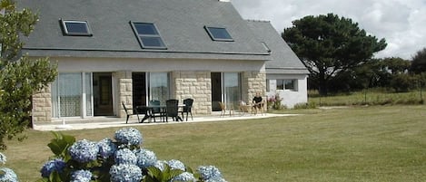 A two-story house with a stone facade, a covered patio with outdoor furniture, and a well-maintained lawn.