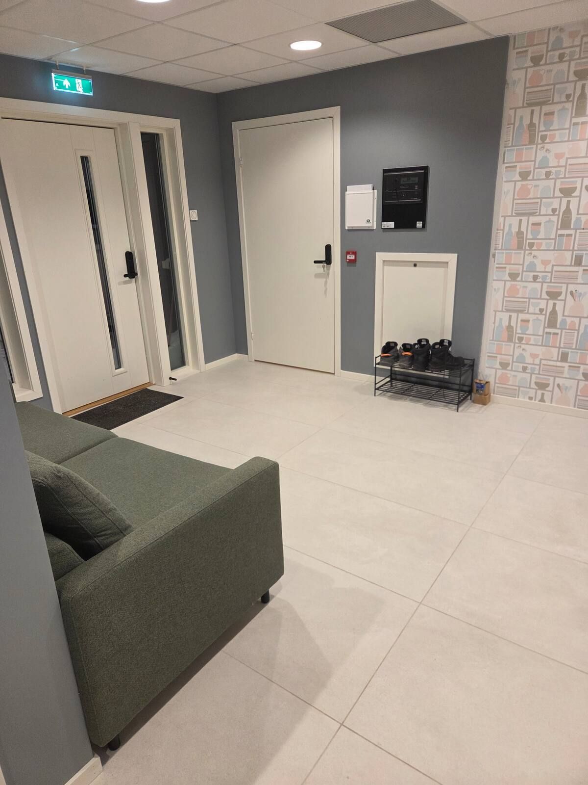 A reception area with a green sofa, a shoe rack, and a door with an emergency exit sign.