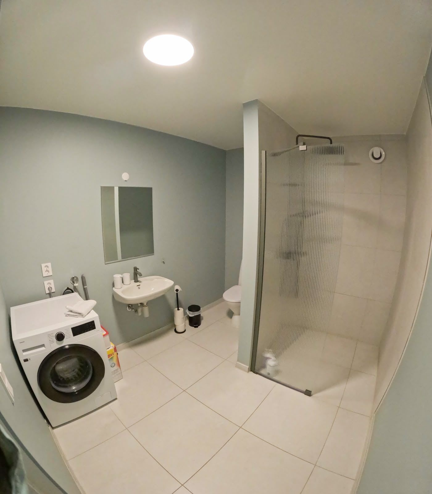 A bathroom with a washing machine, sink, toilet, and a glass shower enclosure.