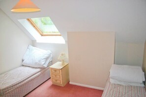 Une petite chambre à coucher composée d’une seule pièce, avec deux lits simples, une table de chevet, une lampe et une lucarne.