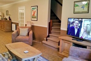 Ett vardagsrum med en soffa, ett soffbord, en tv, en trappa och en dörr.