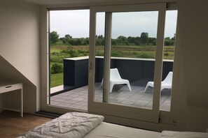 A bedroom with a large sliding glass door leading to an outdoor balcony with two white chairs. - Holiday home in Zeeland with 1 bedroom (Vrouwenpolder)