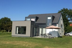 A modern two-story house with a flat roof, large windows, and a patio with outdoor furniture. - Holiday home in Zeeland with 1 bedroom (Vrouwenpolder)