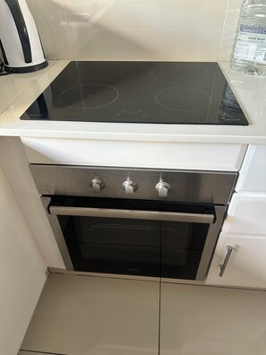Eine Küche mit einer schwarzen Induktionskochplatte, einem Edelstahlbackofen und einer weißen Arbeitsplatte.