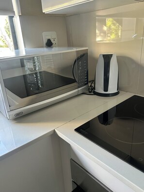 A compact kitchen with a microwave, kettle, and induction cooktop. - Sandton Escape - a luxury one bed apartment in Morningside (Sandton)