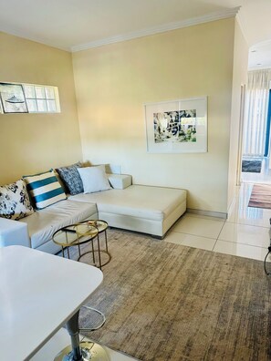 A modern living room with a sofa, a coffee table, and a framed abstract painting on the wall. - Sandton Escape - a luxury one bed apartment in Morningside (Sandton)