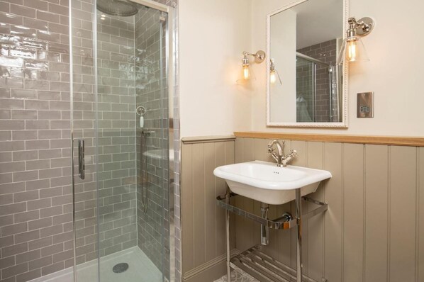 Un baño con cabina de ducha de vidrio, un lavamanos blanco con un solo grifo e iluminación empotrada.