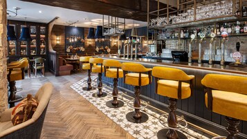 Baarialue, jossa on puiset baarijakkarat, tiski hanoin ja hyllyt pulloineen.