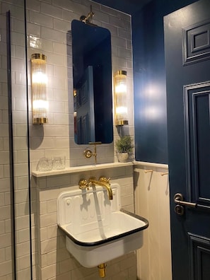 A bathroom with a white sink, gold fixtures, and two wall-mounted lights. - CBH Beadnell Towers & Kitchen (Chathill)