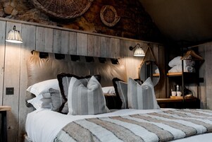 A bedroom with a wooden headboard, two bedside lamps, a bed with striped bedding, and a shelf with towels.