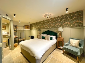 A well-lit bedroom with a large bed, a nightstand, a chair, and a wall with floral wallpaper. - CBH Beadnell Towers & Kitchen (Chathill)