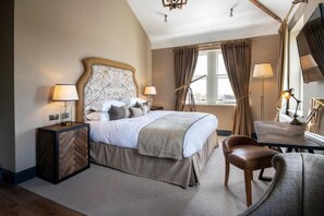 Una habitación de hotel con una cama, lámparas de noche, una silla, una mesa y un televisor.