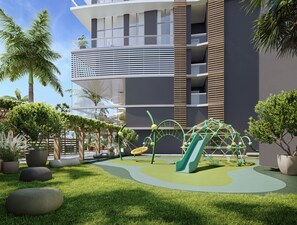 A modern playground with slides and climbing structures, surrounded by grass and potted plants, with a building featuring balconies in the background. - King Suite | Rooftop Views | Theatre Lawn | Pool | Gym | Nexo Miami by AvantStay (North Miami Beach)