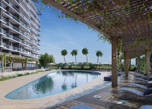 Una piscina con terraza de madera, sillas de descanso y una zona cubierta con plantas.