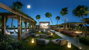 Un área de descanso al aire libre con piscina, asientos y una gran pantalla que muestra una escena.
