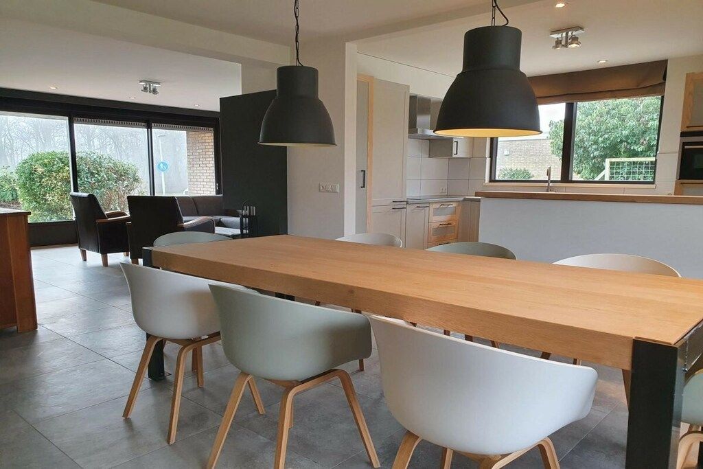 A modern kitchen with a wooden table and chairs, large pendant lights, and a view of the outdoors.