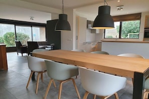 A modern kitchen with a wooden table and chairs, large pendant lights, and a view of the outdoors. - Holiday home with 1 bedroom (De Koog, Texel)