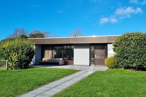 A modern house with a covered patio, a lawn, and a pathway leading to the entrance. - Holiday home with 1 bedroom (De Koog, Texel)