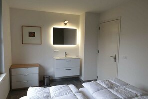 A hotel room with a bed, a bedside table, a small cabinet, a mirror, and a door. - Holiday home with 1 bedroom (De Koog, Texel)