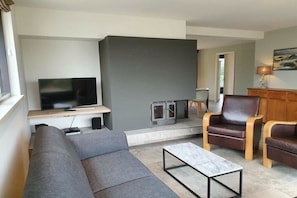 A modern living room with a flat-screen TV, a sofa, two leather armchairs, a coffee table, and a fireplace. - Holiday home with 1 bedroom (De Koog, Texel)