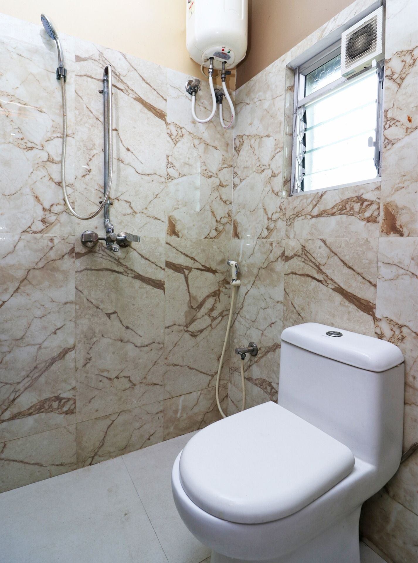 Un baño con inodoro, ducha con cabezal de ducha manual y calentador de agua instalado en la pared.