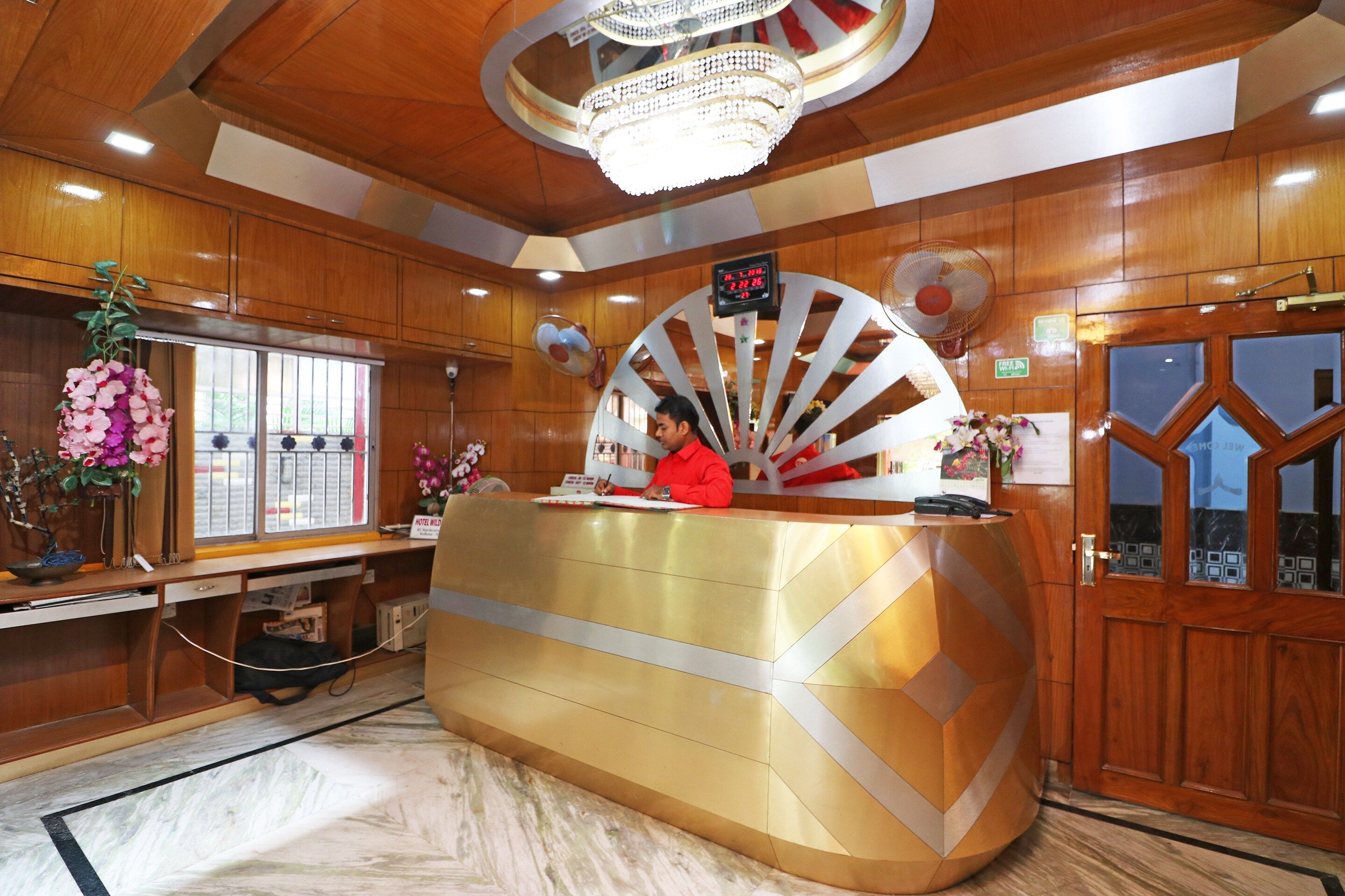 A hotel reception desk with a digital clock, a fan, and a decorative fan on the wall.