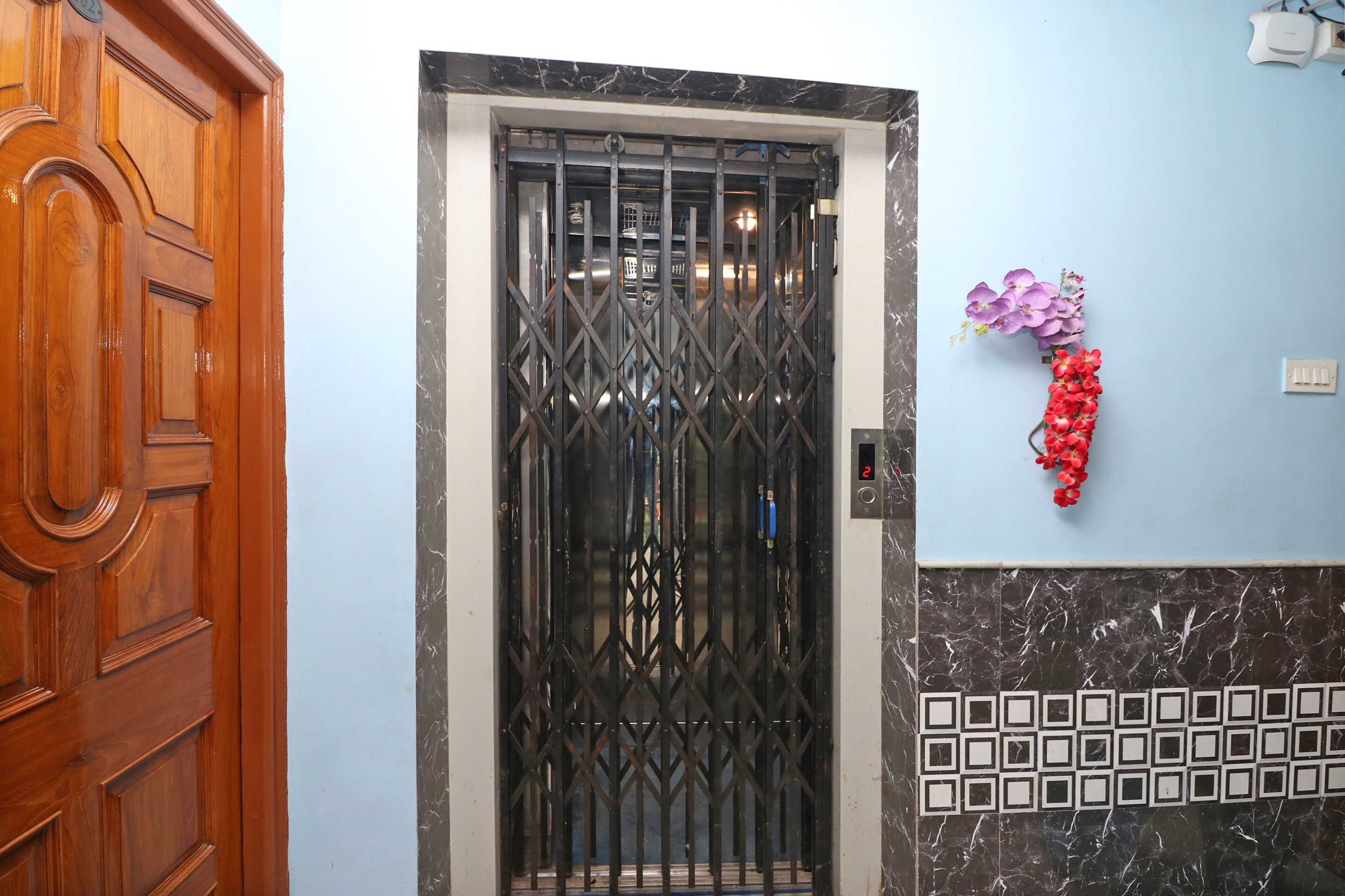 Una puerta de madera, un portón de metal y una pared con un interruptor de luz y flores decorativas.