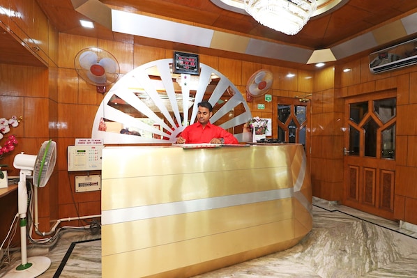Mostrador de recepción de hotel con un ventilador grande, un reloj y un cartel que indica horarios de registro de entrada y salida.